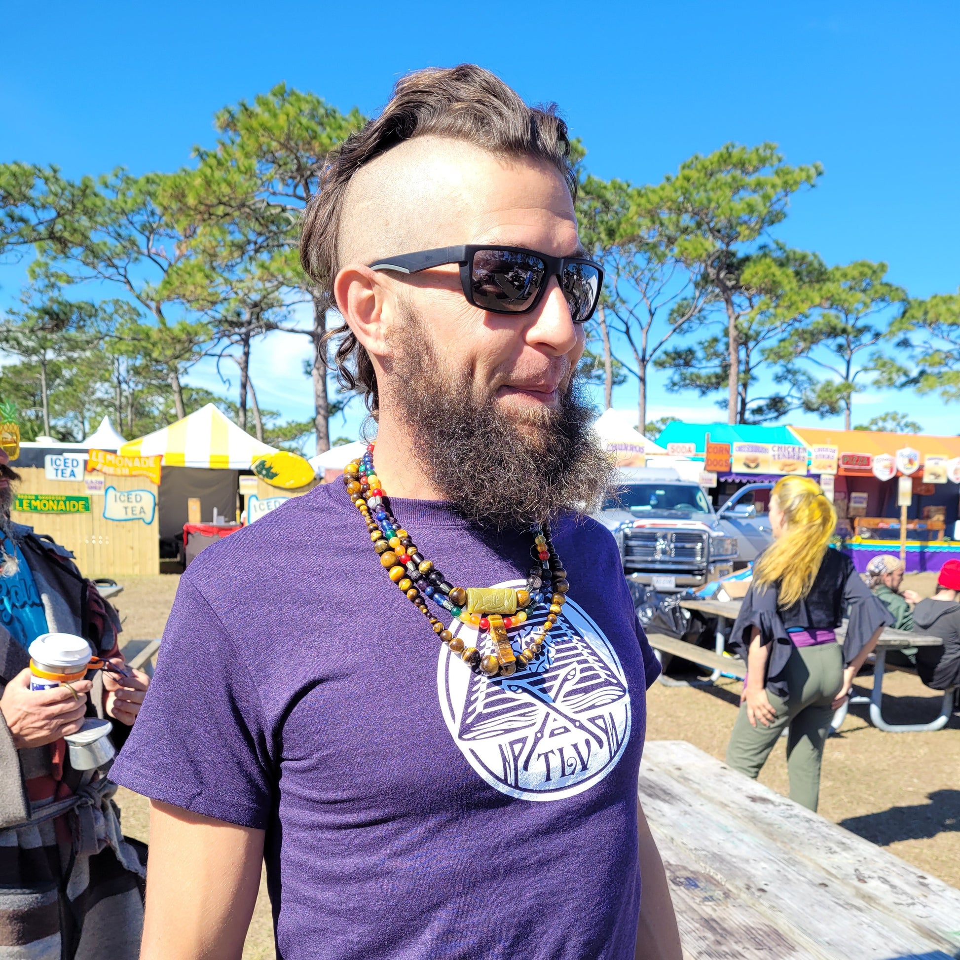Person wearing a purple shirt with a logo outdoors on a sunny day